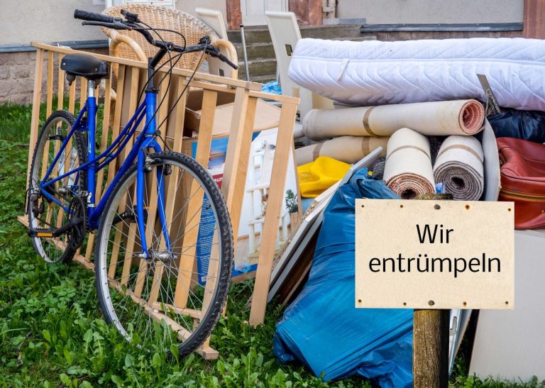 Ein blauer Fahrrad steht neben verschiedenen Möbeln und einer Beschilderung „Wir entrümpeln“.